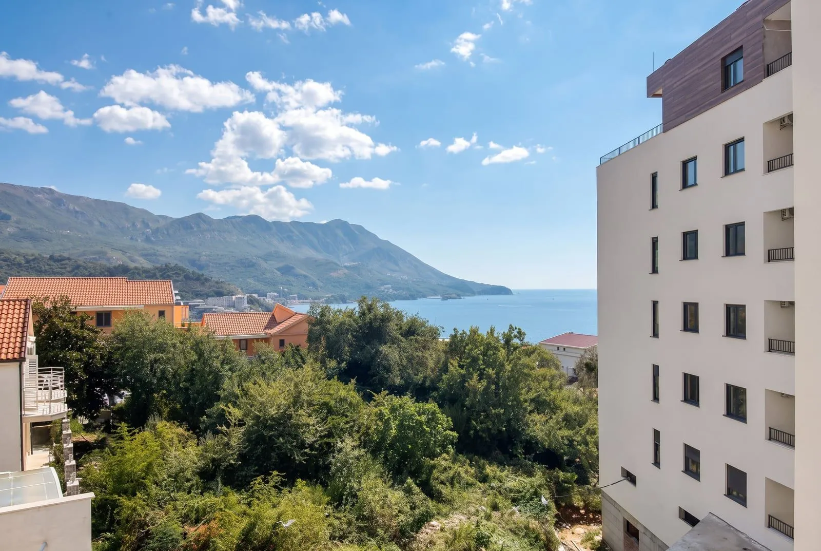 Pogled sa terase na more, planine i okolne zgrade sa zelenilom.
