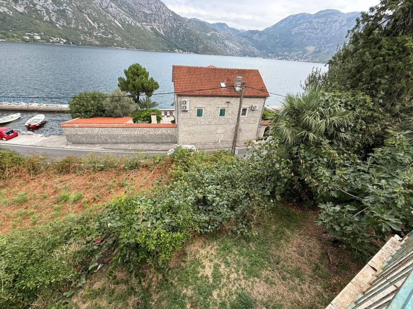Pogled na kamenu kuću uz obalu mora i planine u pozadini.