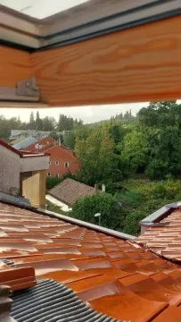 View from a roof window overlooking house roofs and green areas. - image 3