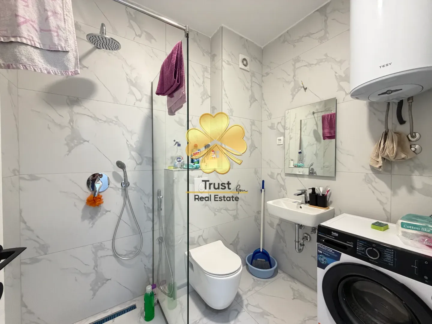 Compact bathroom with a shower cabin, sink, and washing machine.