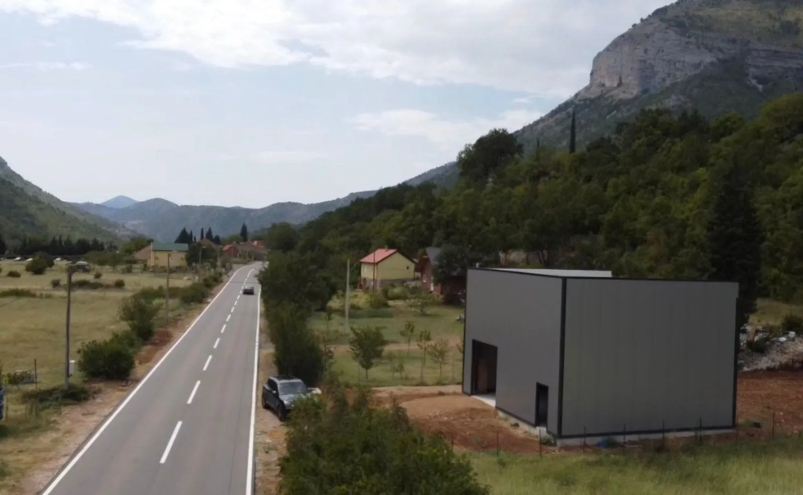 Aerial view of a modern building next to the road and mountain landscape.