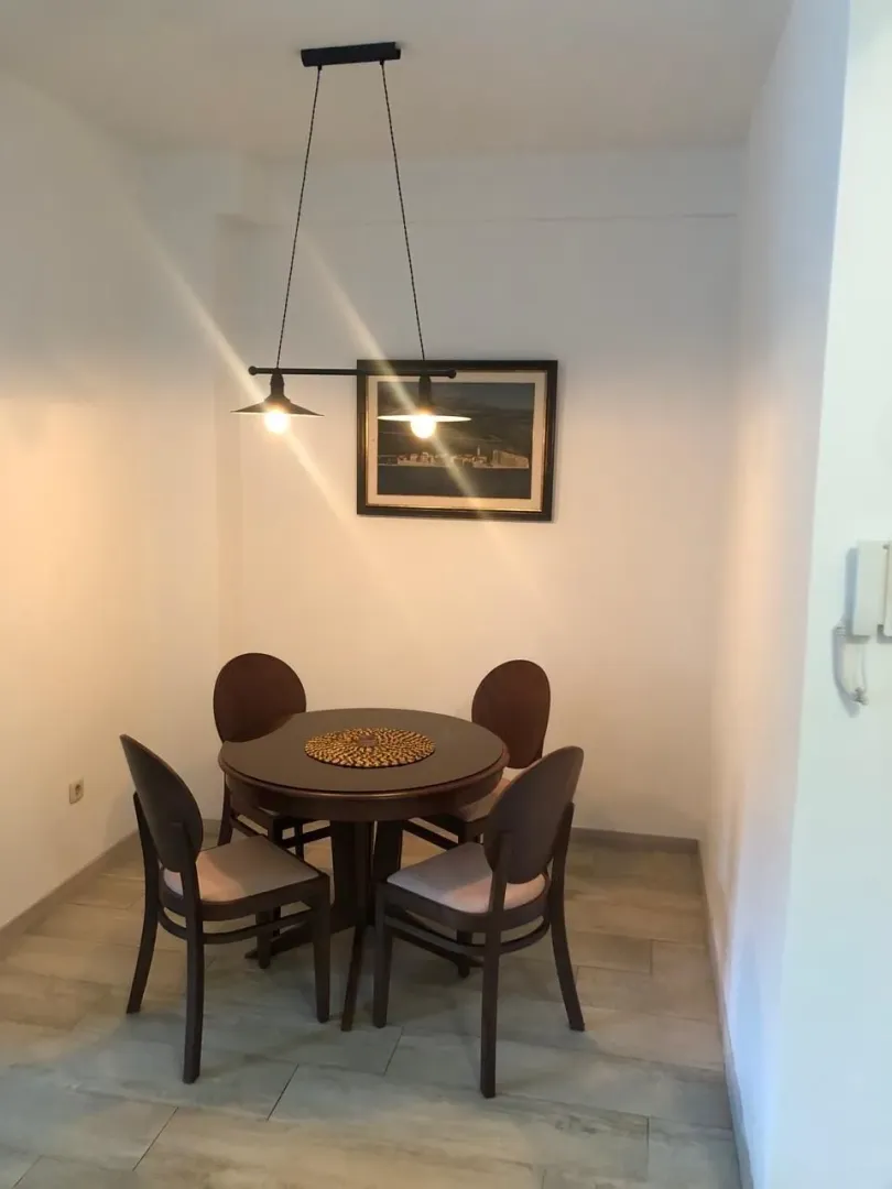 Dining area with a round table, four chairs, and a hanging lamp.