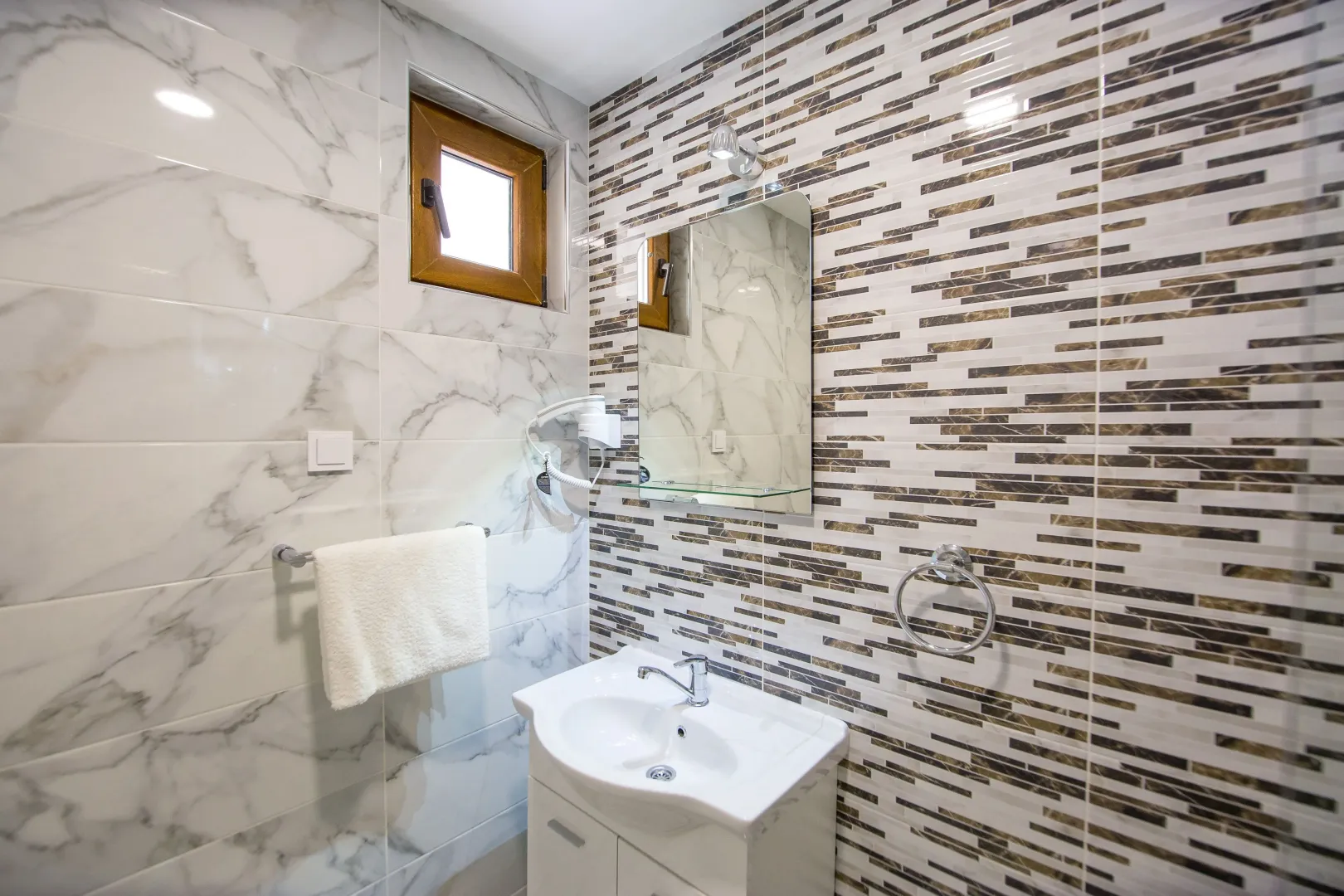 Modernly equipped bathroom with a washbasin, mirror, and tiles.