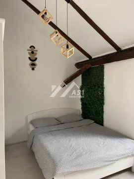 Spavaća soba sa bračnim krevetom, kosim krovom sa drvenim gredama i modernim visilicama. - image 4