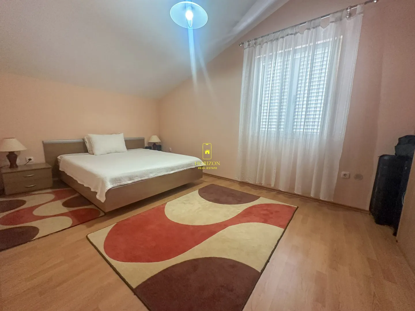 Prostrana spavaća soba sa bračnim krevetom, tepisima i prozorom.