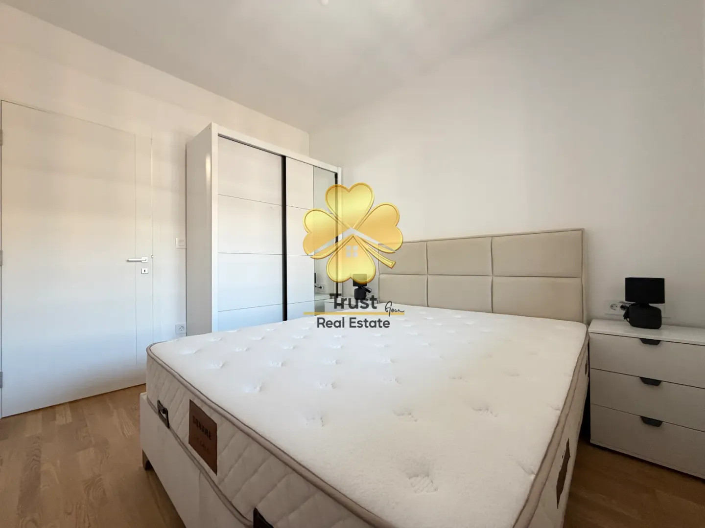 Bright bedroom with a double bed, white wardrobe, and a bedside table.