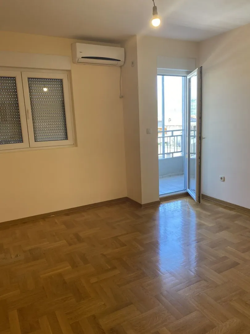 Prazna soba sa parketom, klima uređajem i izlazom na balkon.