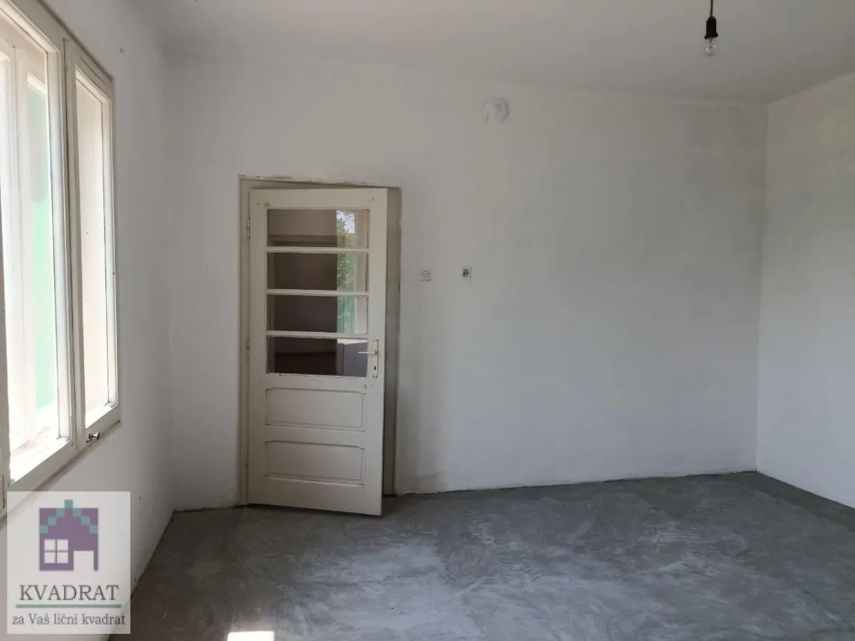 Prazna neuređena prostorija sa belim zidovima, prozorom i vratima.