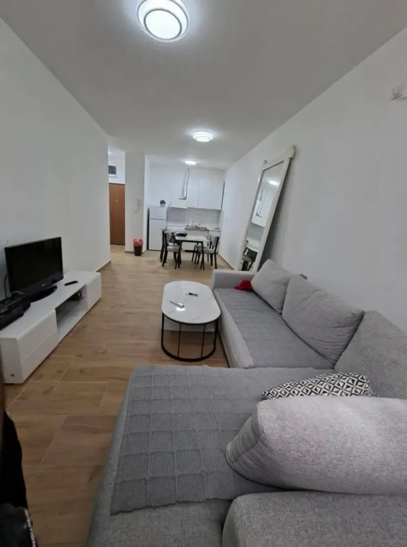 Dnevna soba sa garniturom i televizorom, sa pogledom na trpezariju i kuhinju.