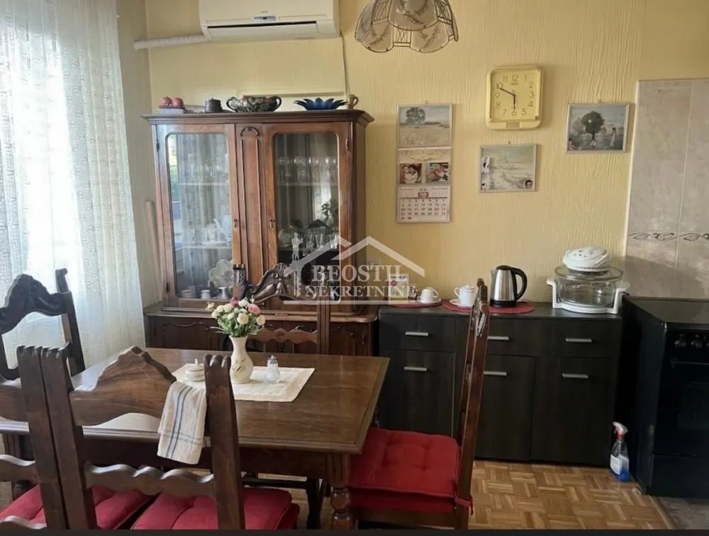 Trpezarija sa drvenim stolom i vitrinom u sklopu kuhinje.