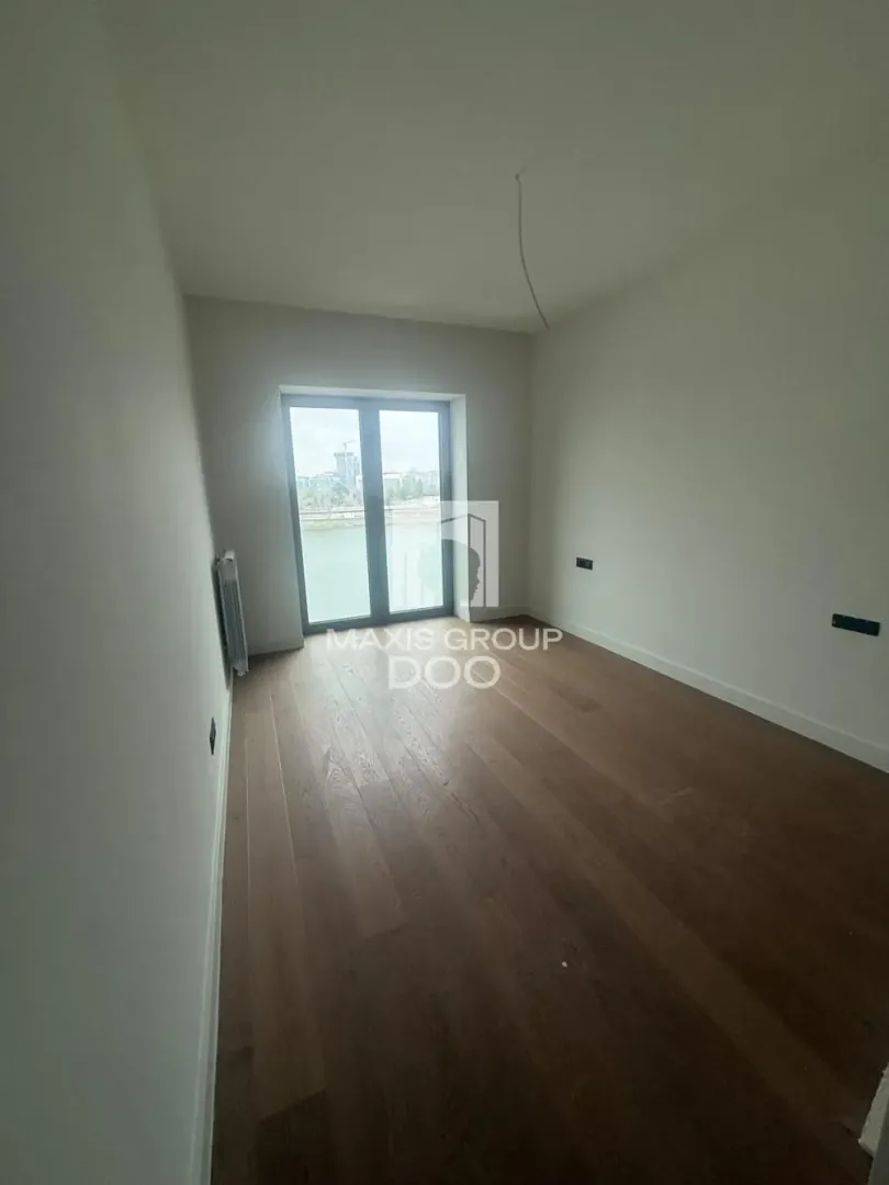 Empty unfurnished room with wooden flooring and balcony doors.