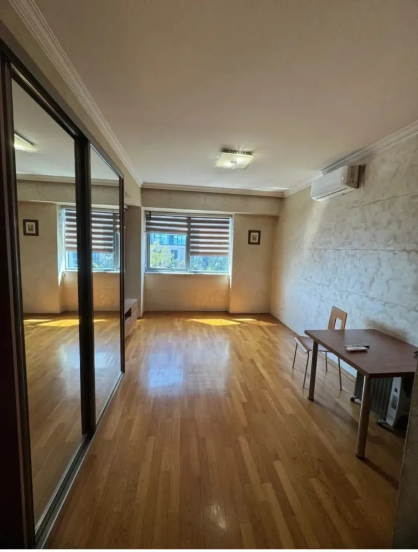 Spacious living room with wooden flooring, a large mirrored wardrobe, and a dining table.