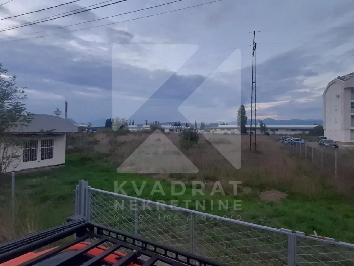 Pogled na plac sa niskim rastinjem i okolnim zgradama.