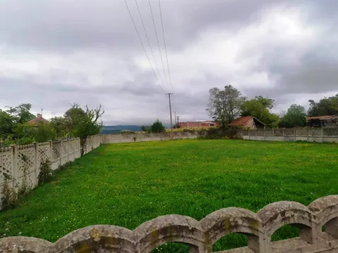 Ograđeno travnato dvorište sa stablima i okolnim kućama u pozadini. - image 2
