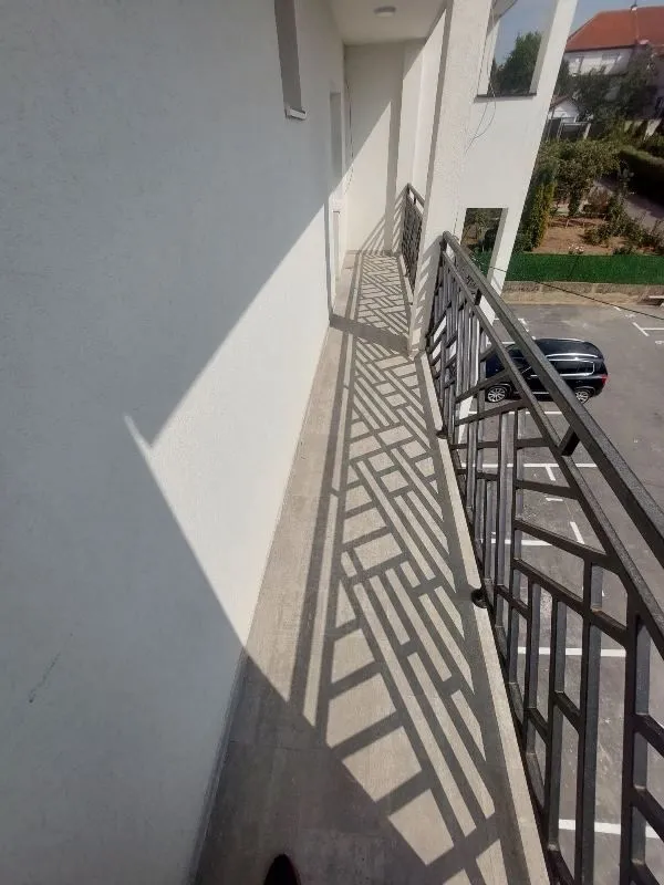 Dugački balkon sa metalnom ogradom i pogledom na parking.