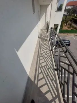 Dugački balkon sa metalnom ogradom i pogledom na parking. - image 9