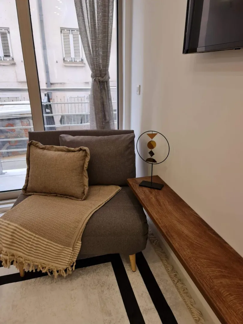 A comfortable armchair with pillows and a wooden shelf by the window in the living room.