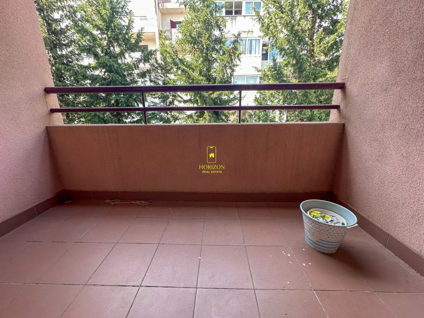 Natkriveni balkon sa popločanim podom i pogledom na zelenilo.