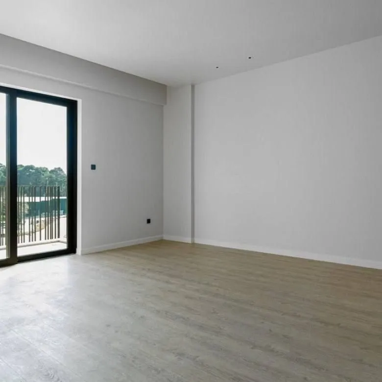 Prazna svijetla prostorija sa parketom i izlazom na balkon.