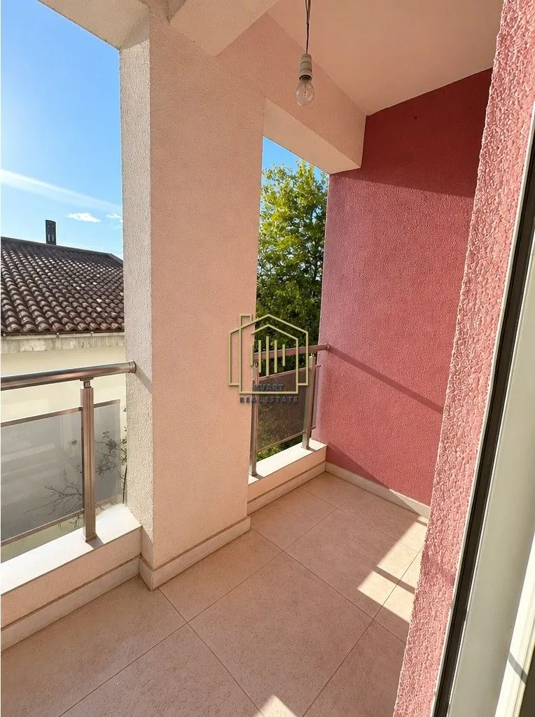 Natkriveni balkon sa popločanim podom i metalnom ogradom.