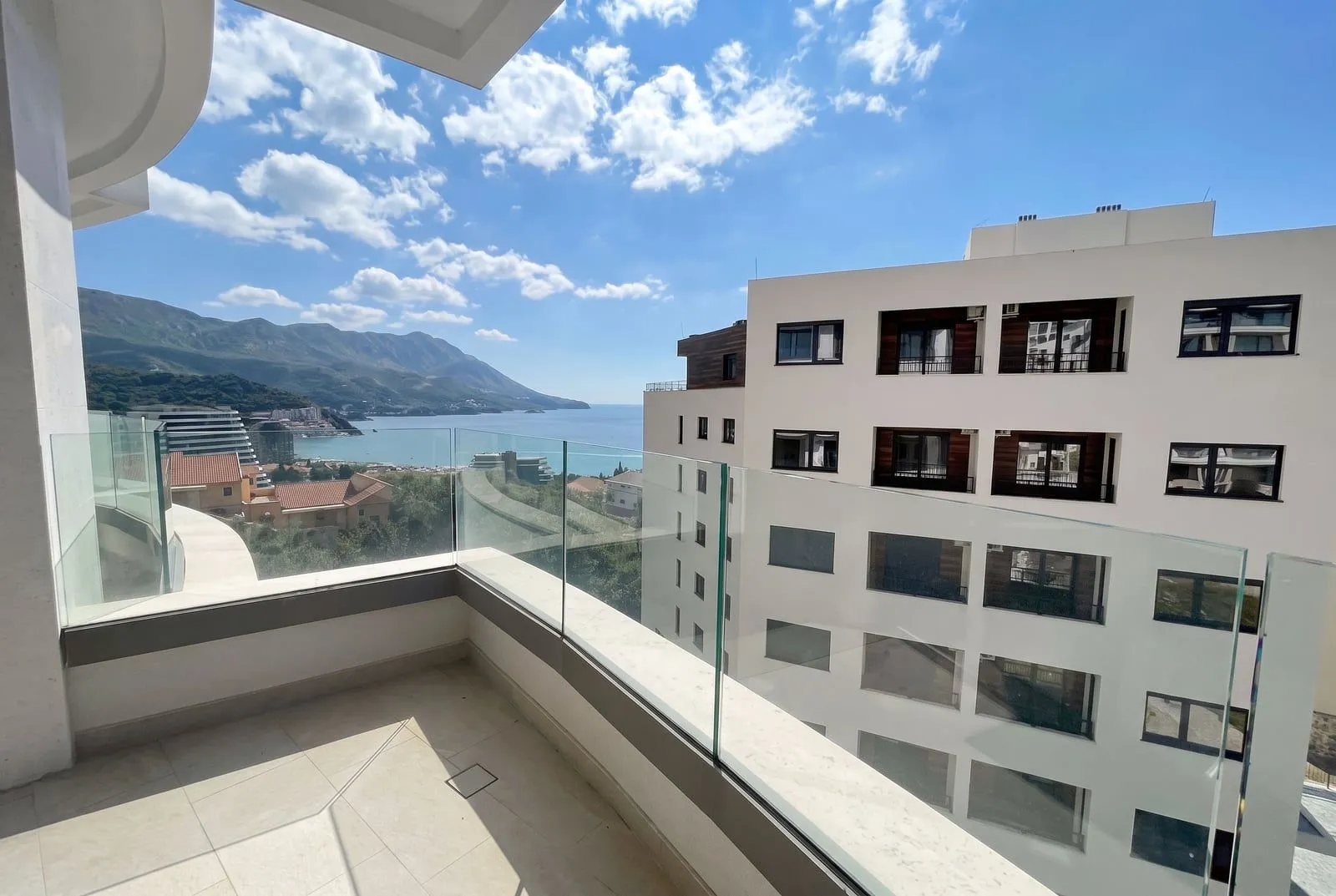 Moderan prostrani balkon sa staklenom ogradom i pogledom na more i planine.
