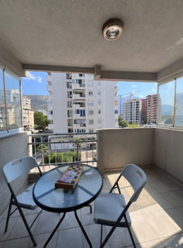Natkriveni balkon sa garniturom za sjedenje i pogledom na okolne zgrade.