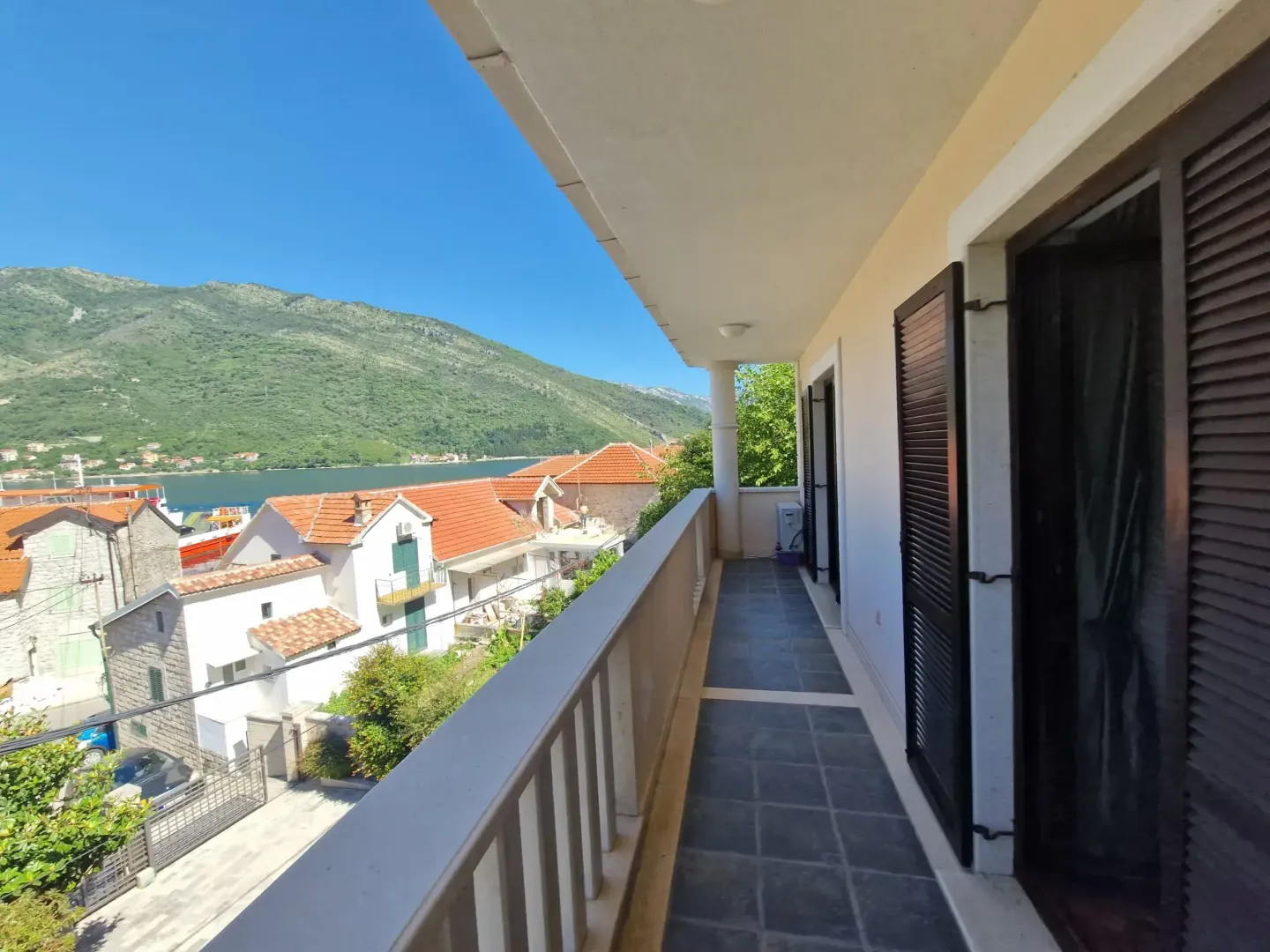 Dugačka popločana terasa sa pogledom na more i okolne planine.