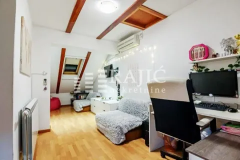 Attic room with a desk, sofa, and wooden ceiling beams. - image 9