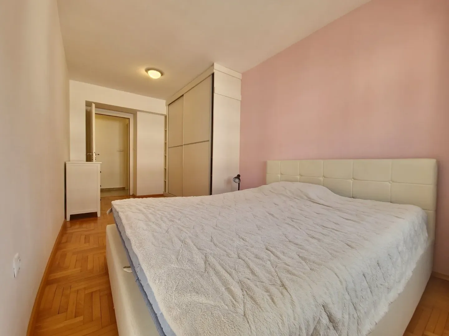 Bedroom with a large double bed, wardrobe, and parquet flooring.