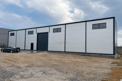 View of the exterior of an industrial warehouse with large doors and unpaved parking area. - image 3