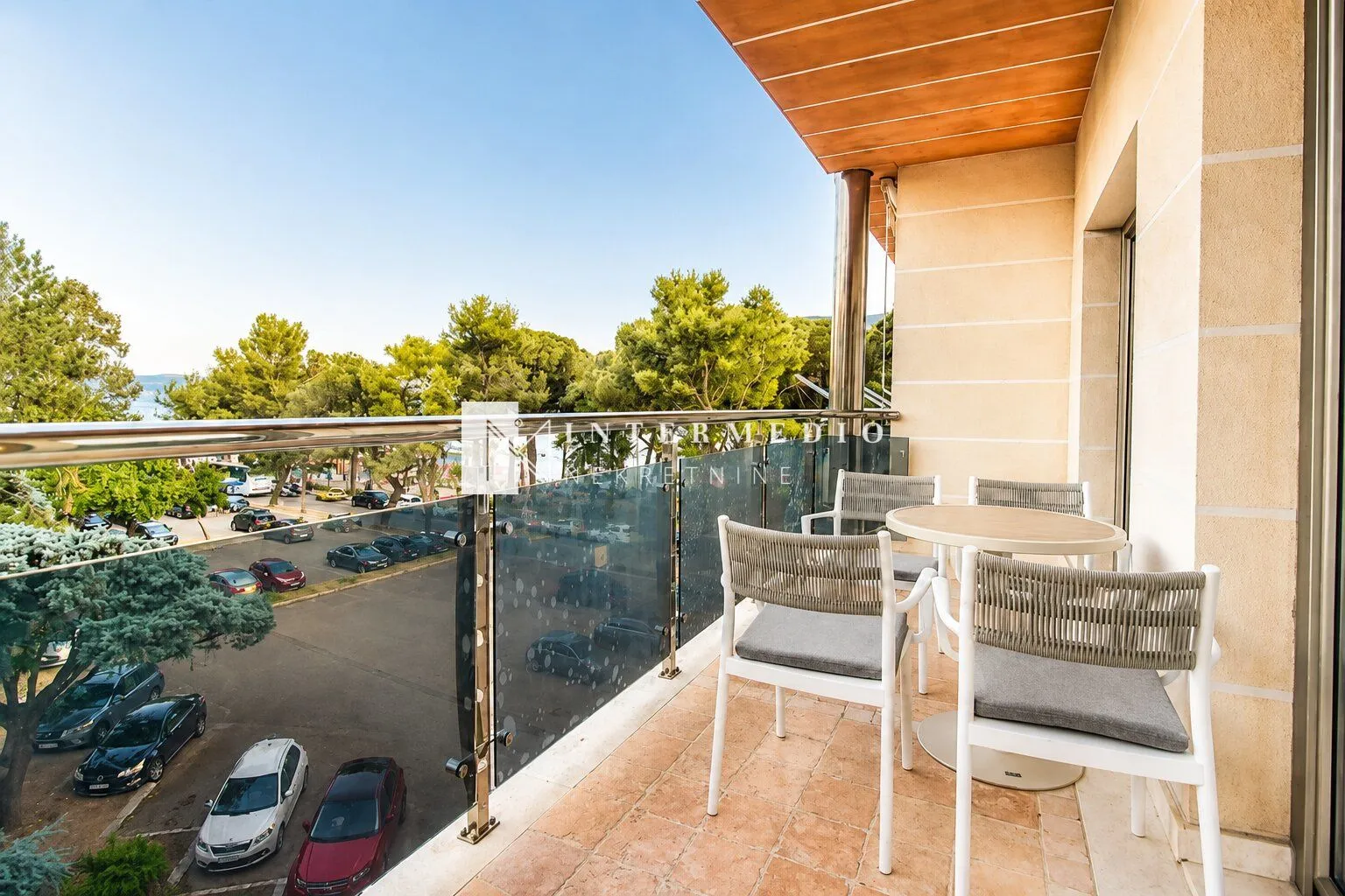 Natkriveni balkon sa garniturom za sedenje i pogledom na ulicu i zelenilo.