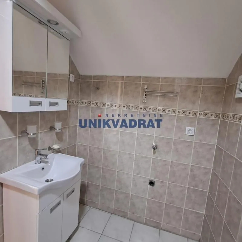Kupatilo obloženo keramičkim pločicama sa umivaonikom i ogledalom.