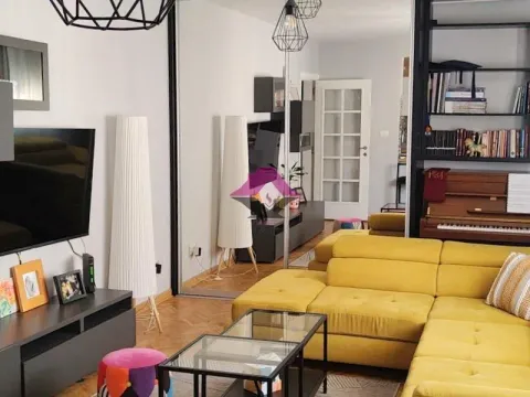 Living room with a yellow sectional sofa, television, and bookshelves. - image 3