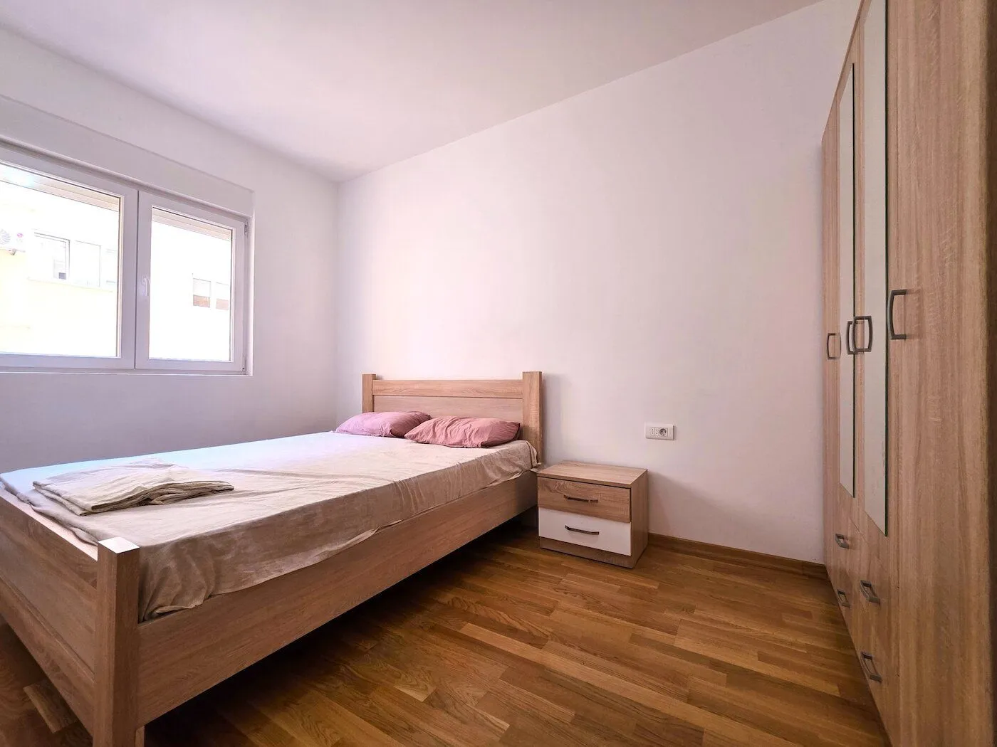 Svjetla spavaća soba sa bračnim krevetom, noćnim stočićem i ormarom.