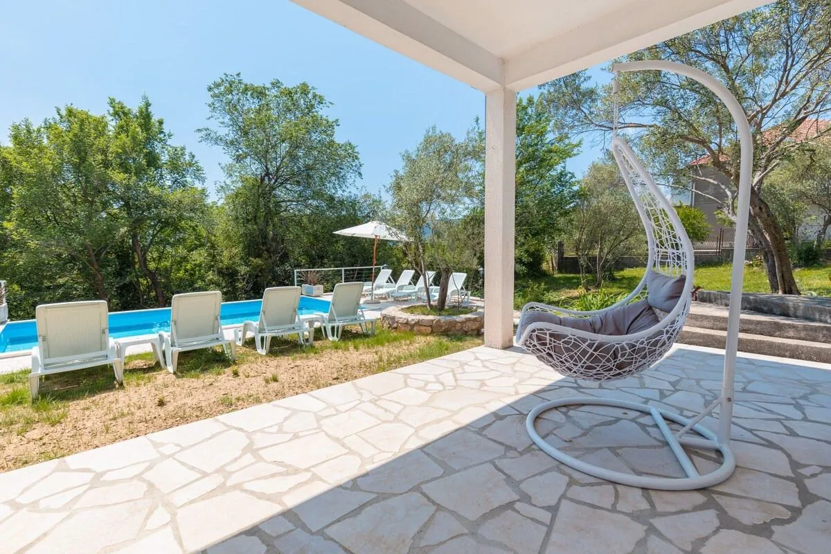 Covered terrace with a hanging chair and a view of the pool and yard.