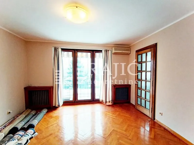 Empty room with parquet flooring, balcony doors, and rolled rugs on the floor.