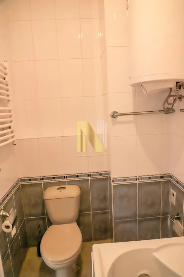 Manje kupatilo sa belim pločicama, toaletom i bojlerom.