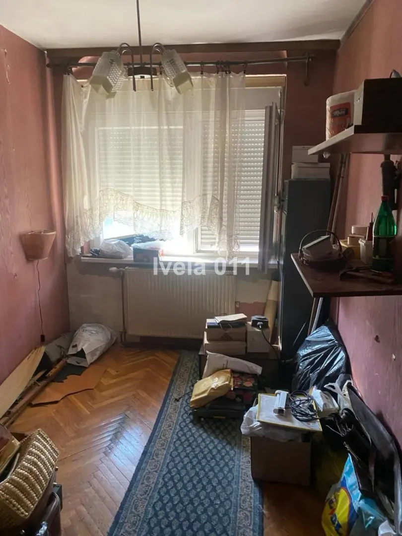 Manja soba sa parketom i prozorom, puna stvari i kutija.