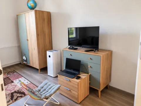 Furnished bedroom with a wardrobe, chest of drawers, television, and a desk with a laptop. - image 3