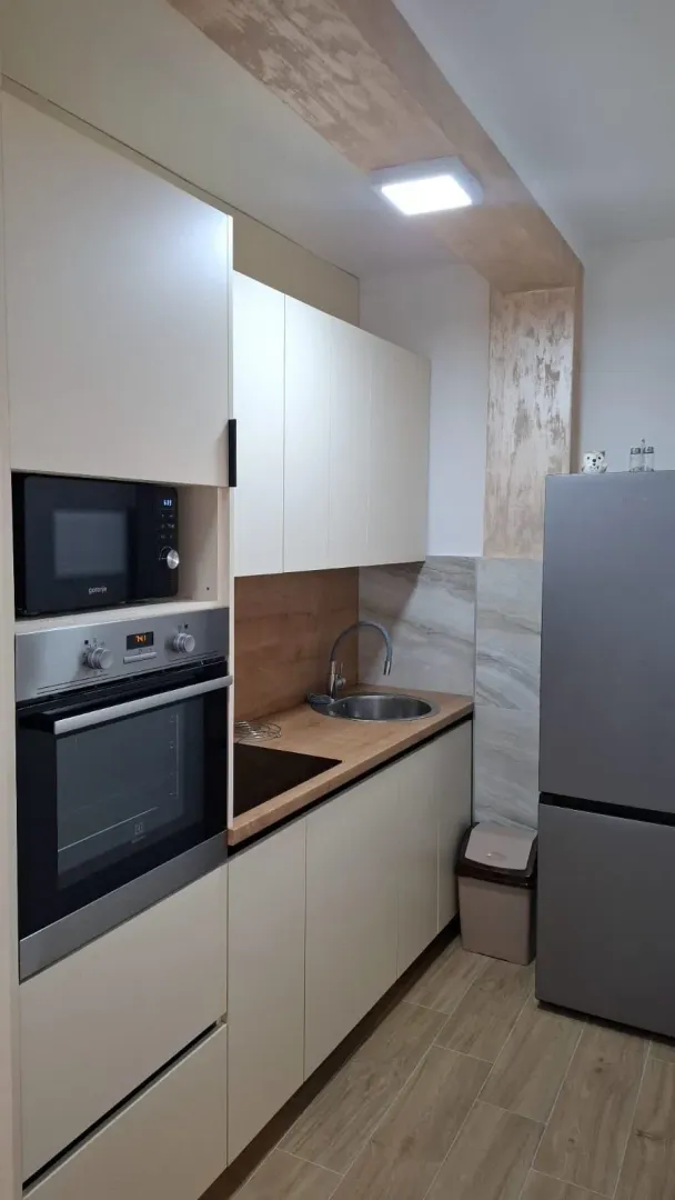 Svijetla moderna kuhinja sa ugradnim aparatima i sivim frižiderom.