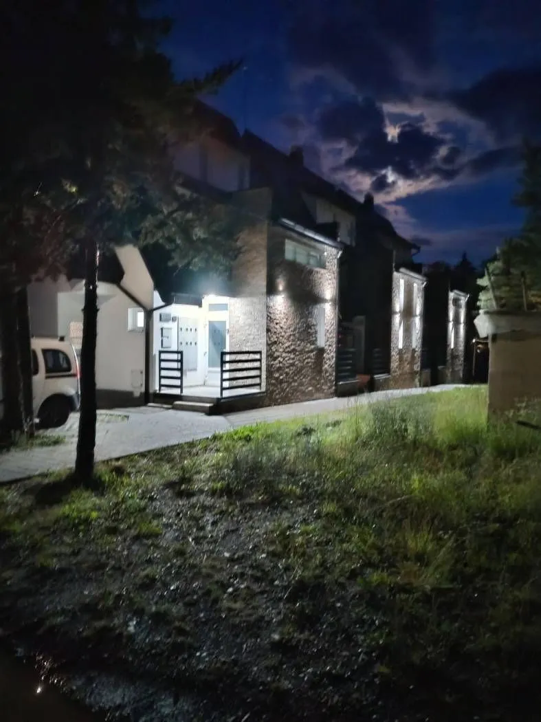 Noćni pogled na spoljašnjost kuće sa osvetljenim ulazom i dvorištem.