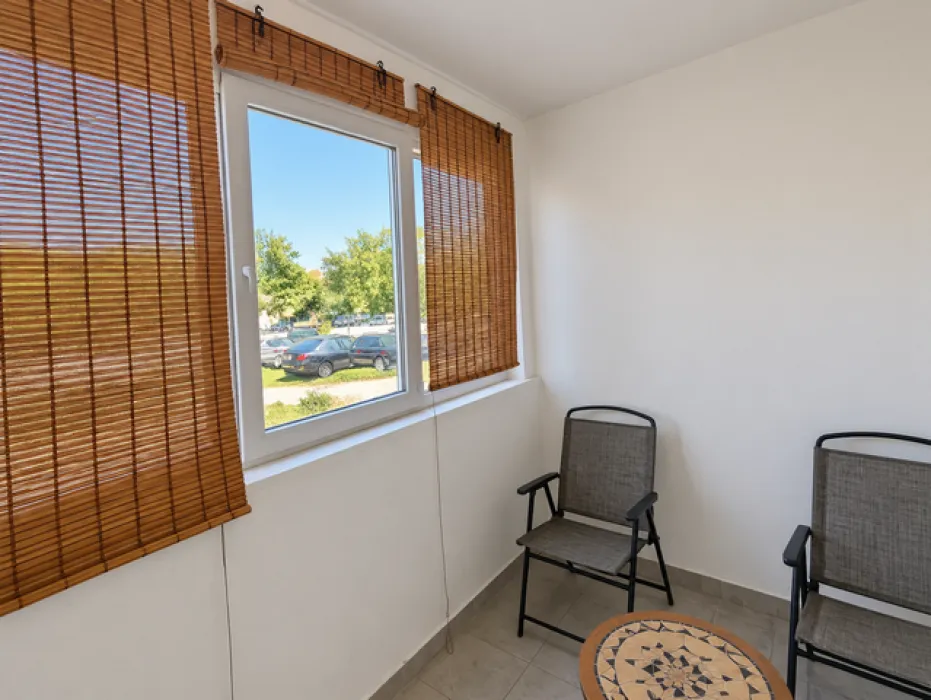 Enclosed balcony with chairs, a small table, and window blinds.