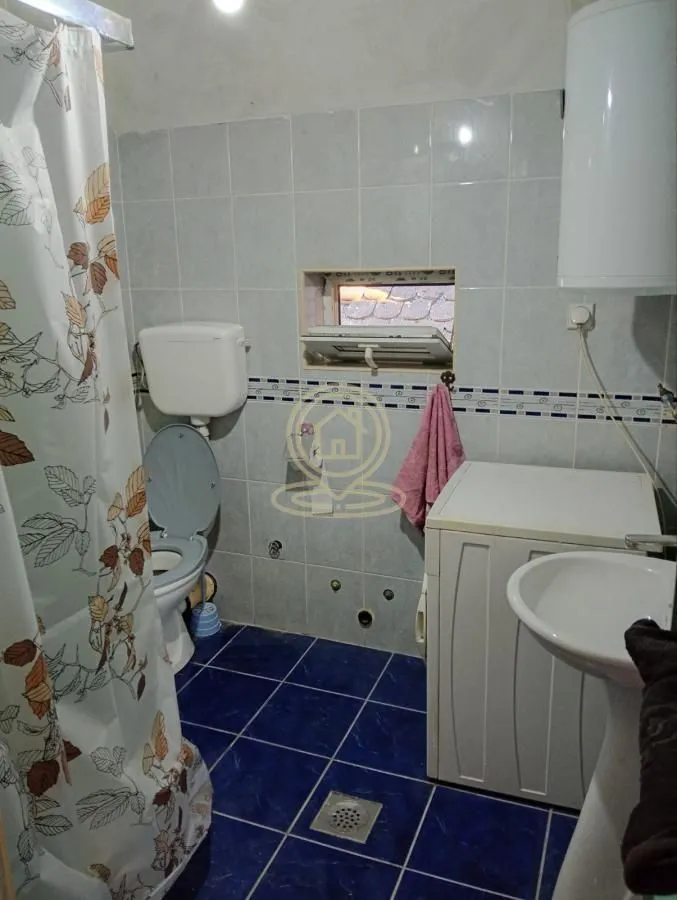 Manje kupatilo sa pločicama, wc šoljom, umivaonikom i veš mašinom.