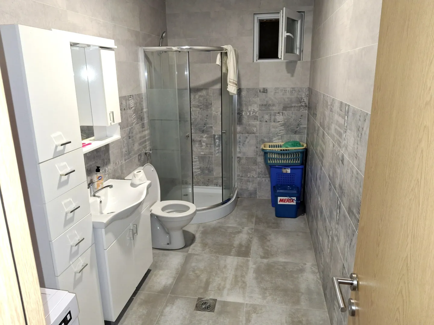 Moderne kupatilo sa tuš kabinom, umivaonikom i bijelim ormarićem.
