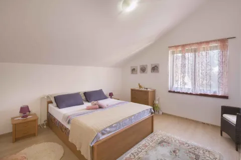Potkrovna spavaća soba sa bračnim krevetom, drvenim komodama i prozorom. - image 2