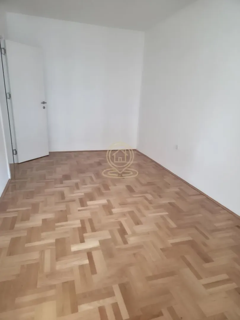 Prazna prostorija sa parketom i belim zidovima.