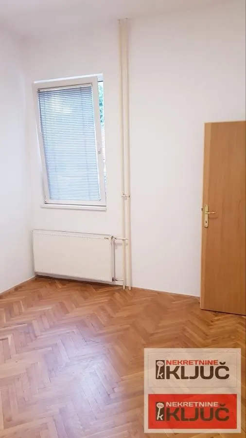 Prazna soba sa parketom, prozorom i drvenim vratima.