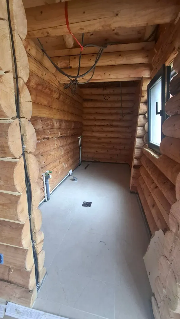 Unfinished room in a wooden house with installations and tiled floor.