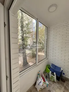 Zastakljena terasa sa belim zidovima od cigle i pogledom na drveće. - image 10