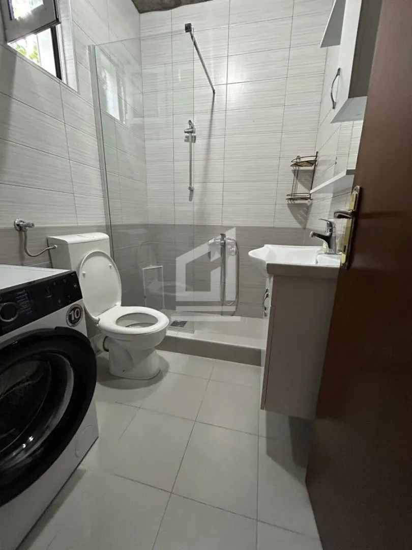 Manje kupatilo sa tuš kabinom, umivaonikom, WC šoljom i veš mašinom.